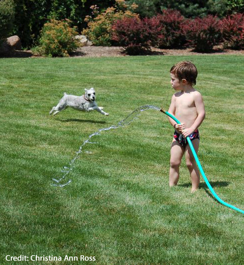 A child pouring water from a hose onto the ground.
