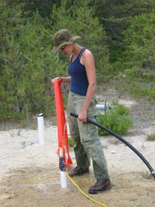[Photo of scientist pouring water into borehole liner]