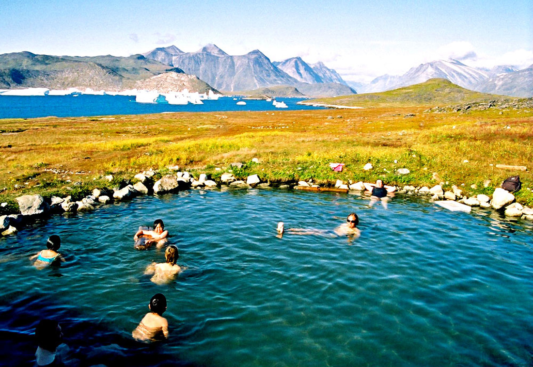 People sitting in a hot spring in Greenland while icebergs float by in the background.